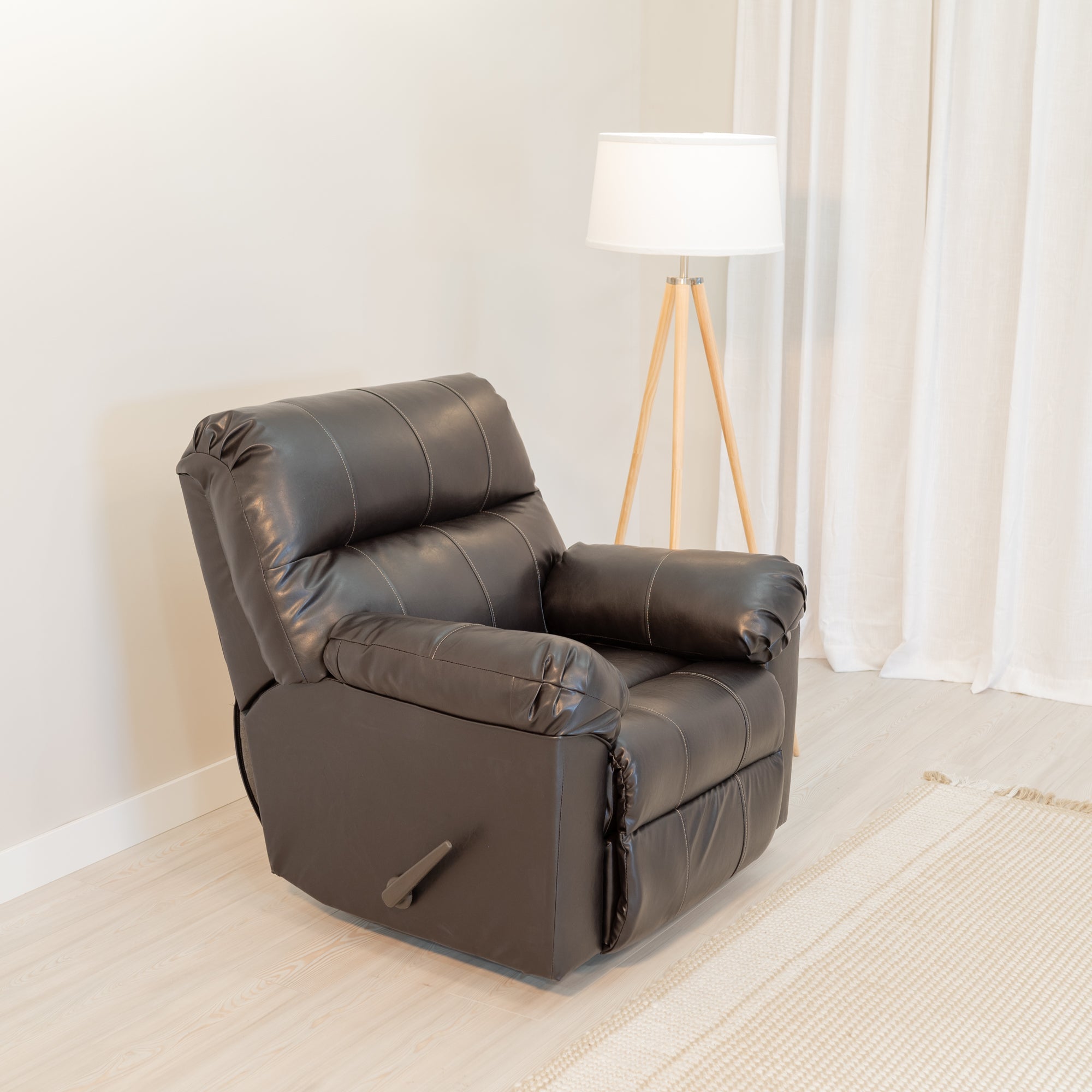 An overstuffed recliner sits in a comfortable looking living room. The upholstery is a dark chocolate brown leather look material with a gentle sheen. a large pull handle can be seen on the side.