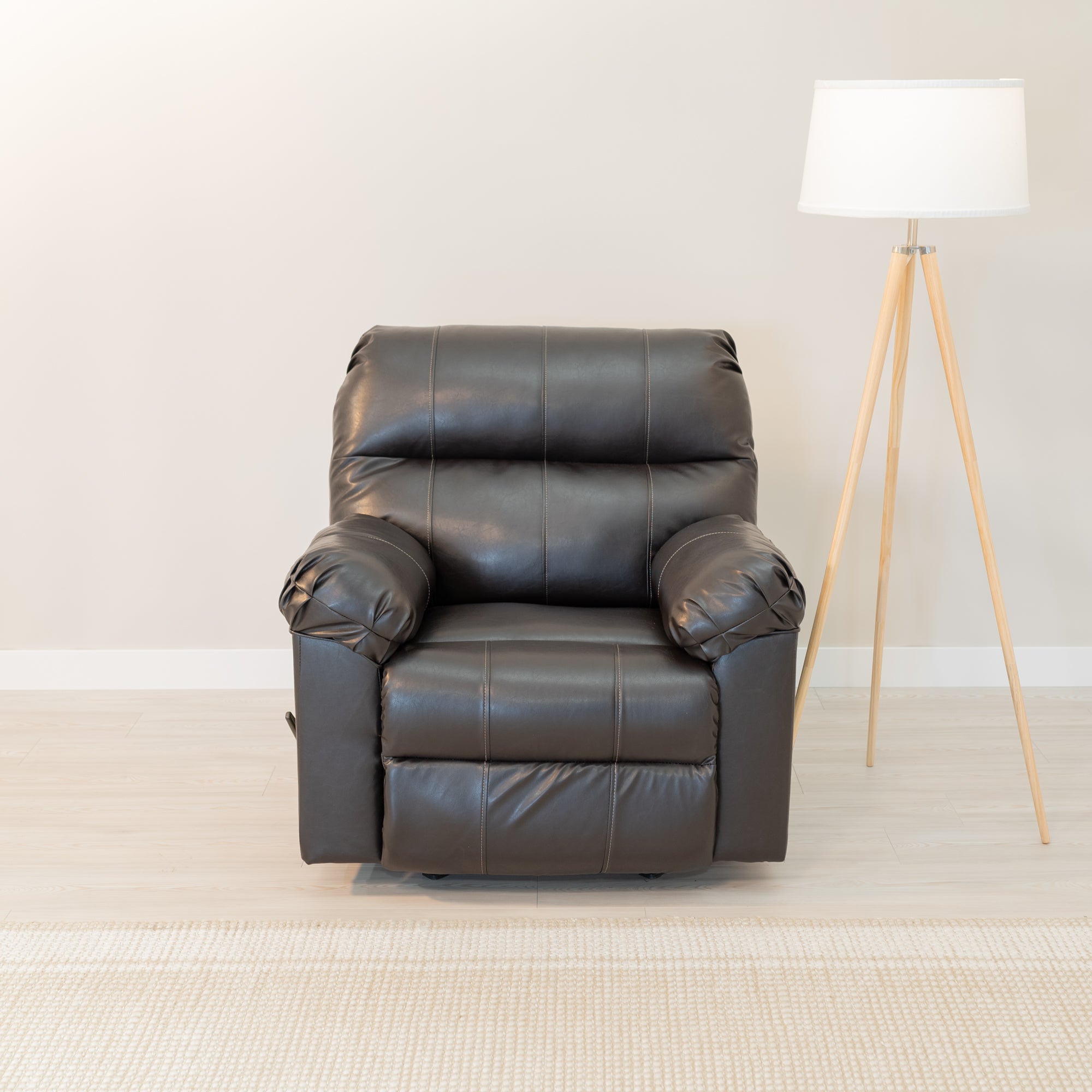 An overstuffed recliner sits in a comfortable looking living room. The upholstery is a dark chocolate brown leather look material with a gentle sheen. a reading lamp is next to the chair