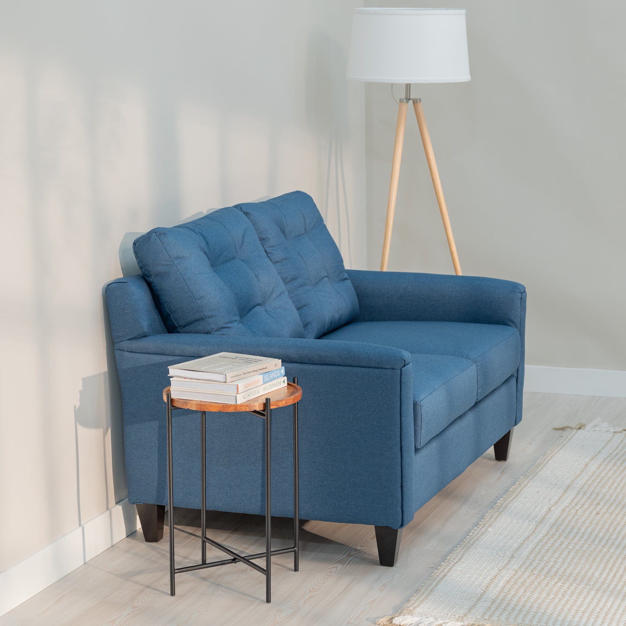 A side view of a denim blue love seat and sofa in a nice looking living room. The sofa and loveseat have clean lines, rectangular arms and a tufted back. the side view shows a gently angled back for a comfortable siting position