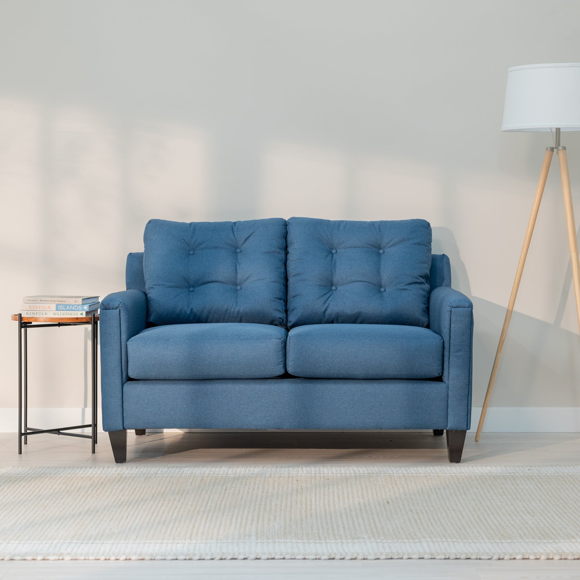 A front view of the denim blue loveseat showing its modern rectangular shape and plush looking tufted back. 