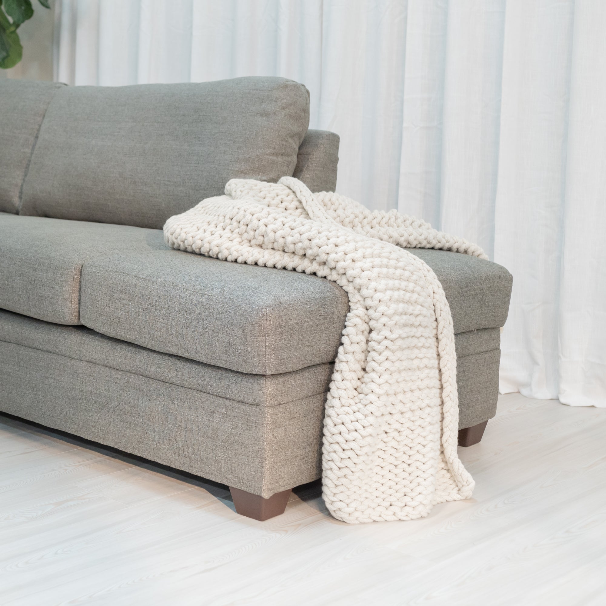 Detailed view of the sofa chase with a chunky blanket draped over the side. It also shows the thick tapered brown rectangular sofa legs. 