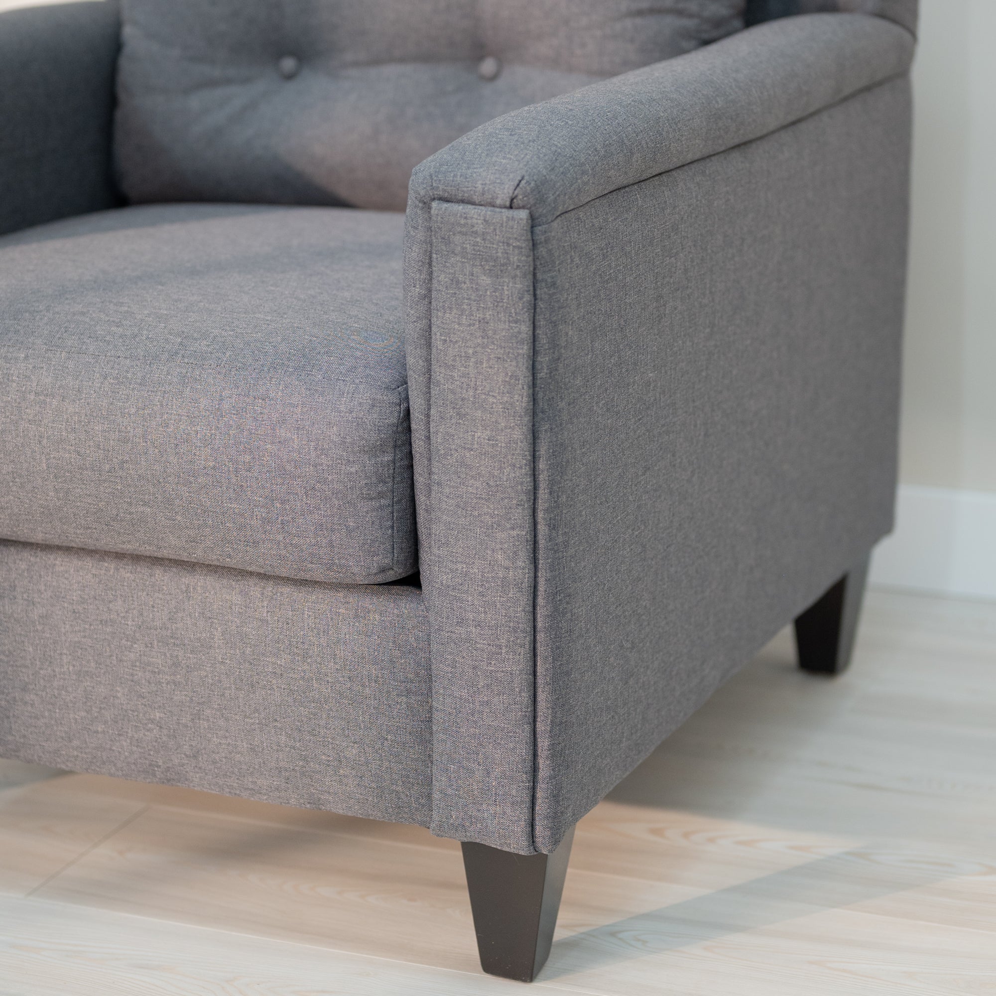 A close up view of the chairs rectangular arm shows the upholstery detailing, and smooth dark surface of the tapered leg. 