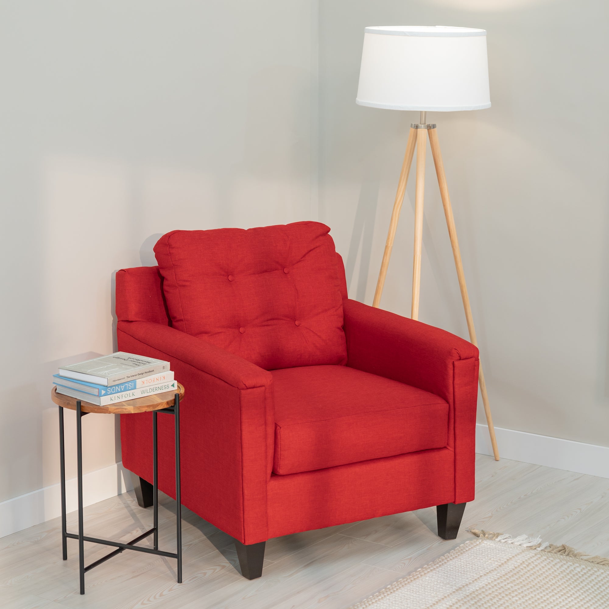 A red accent chair with clean modern lines and a tufted rectangular back sits in a generic living room with a side table and floor lamp. The upholstery fabric is red with lighter colored threads like a denim weave. the chair has tapered dark brown legs .