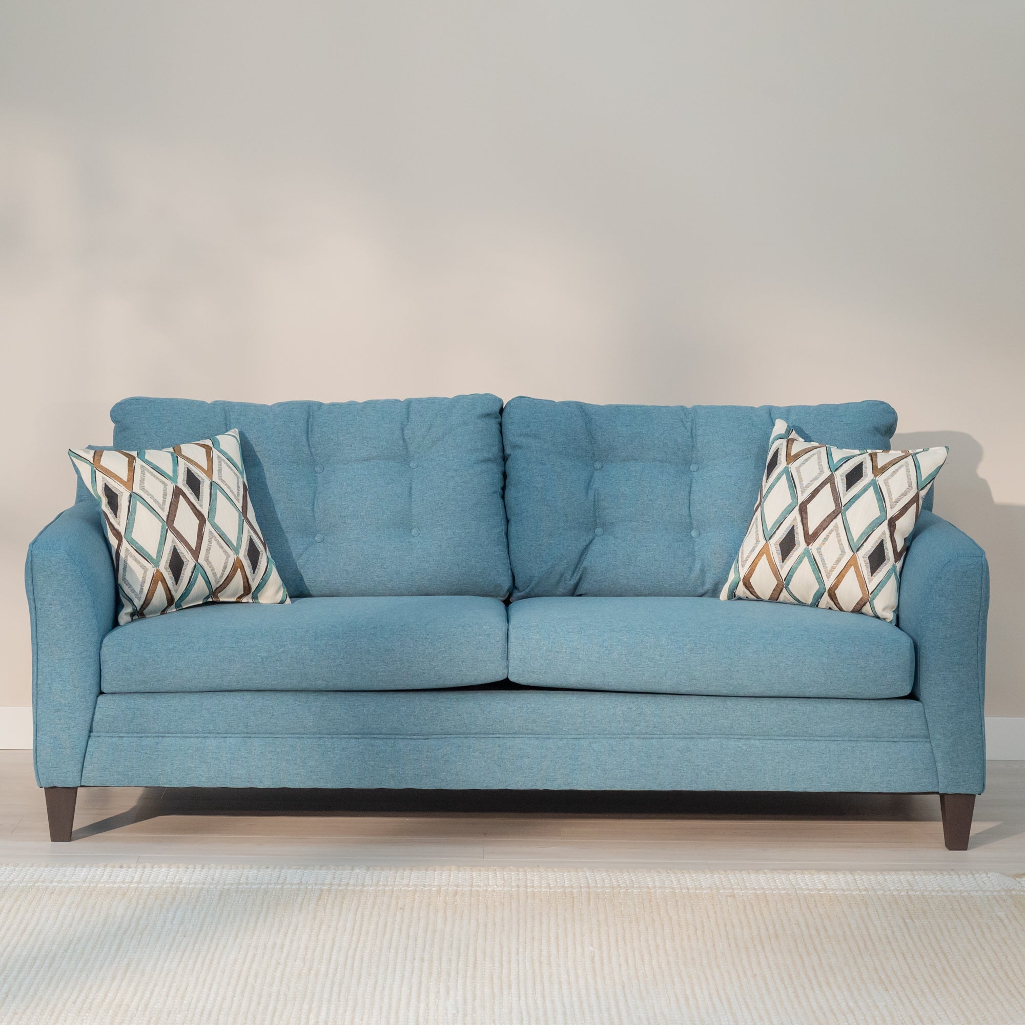 Front view of the sofa with the included throw pillows. The pillows have a hand painted style diamond pattern with teal brown and gold colors on a light cream colored background. 