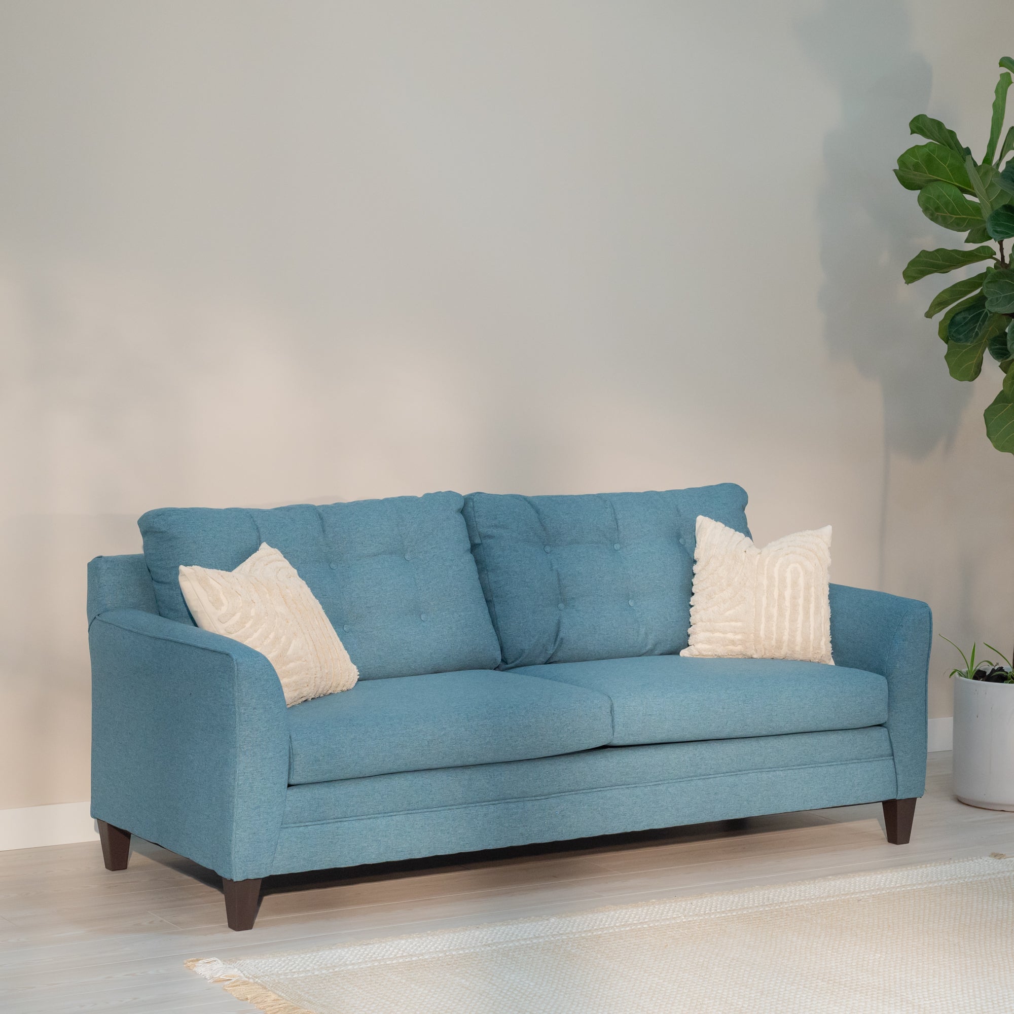 An angled view of the sofa in a light colored living room. the teal stands out against an otherwise boring colored room.