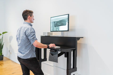 man stands at black ergonomic desk working on a computer 