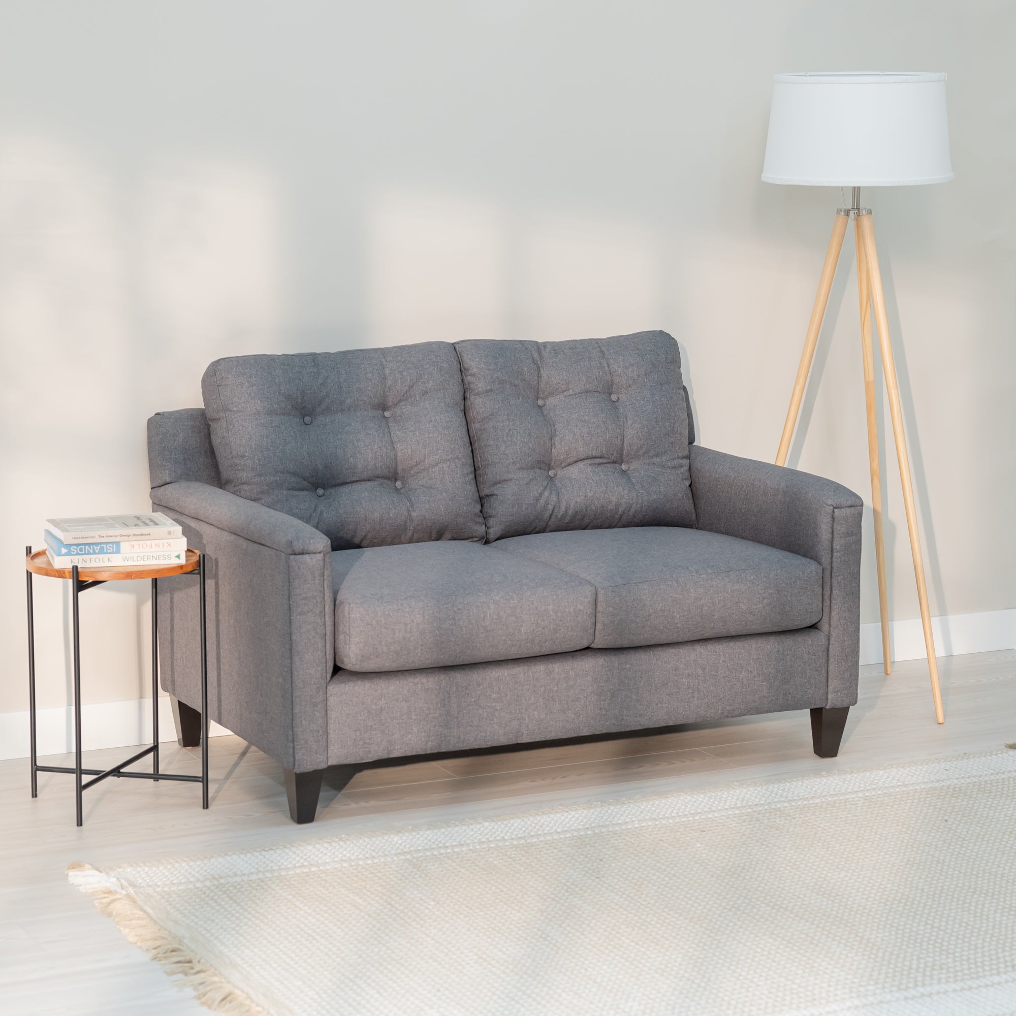 an angled view of the grey loveseat showing its modern rectangular shape and plush looking tufted back.