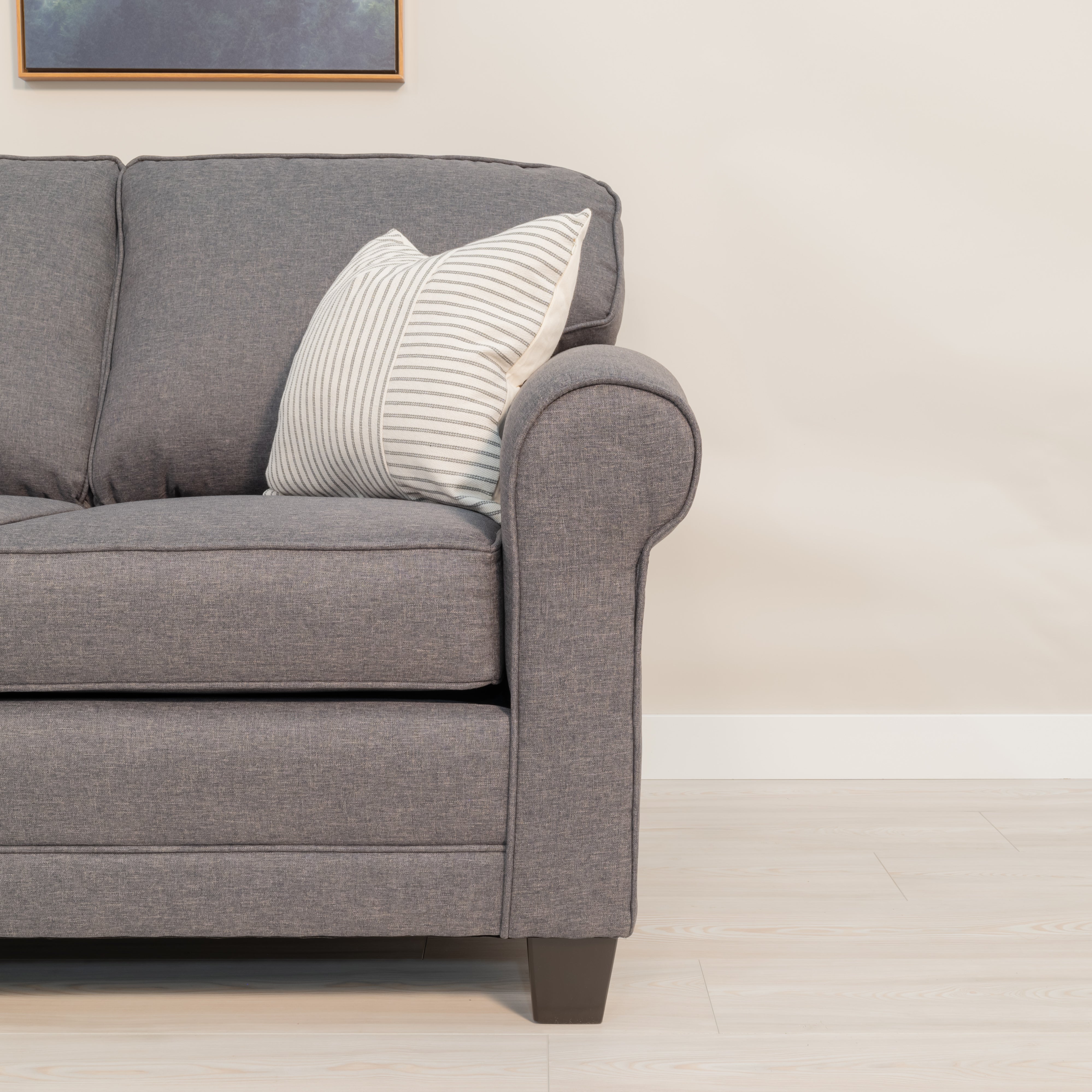 A close up view of the Sheffield sofas rounded arm with round seam piping. The upholstery fabric is grey with lighter colored threads like a denim weave. 